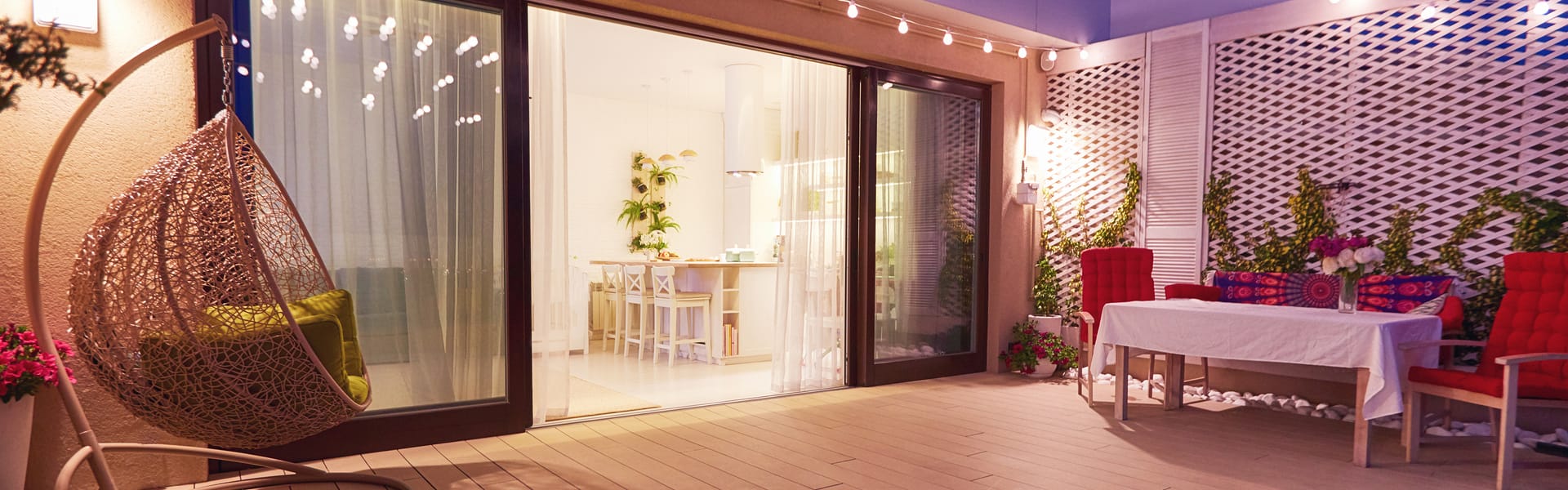 Evening patio with a hanging egg chair, string lights and an outdoor dining setup