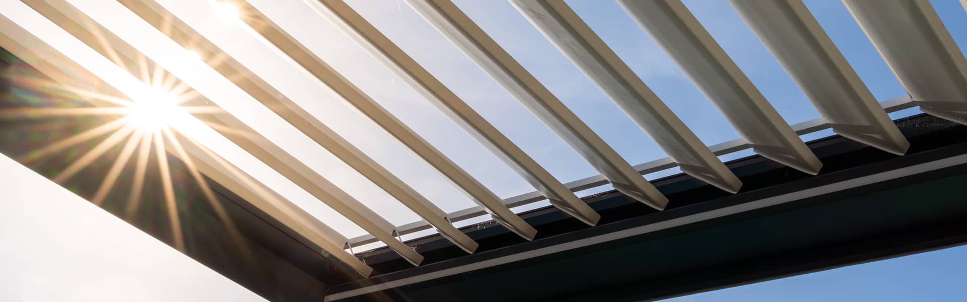 Close-up of an adjustable louvred pergola roof against a blue sky