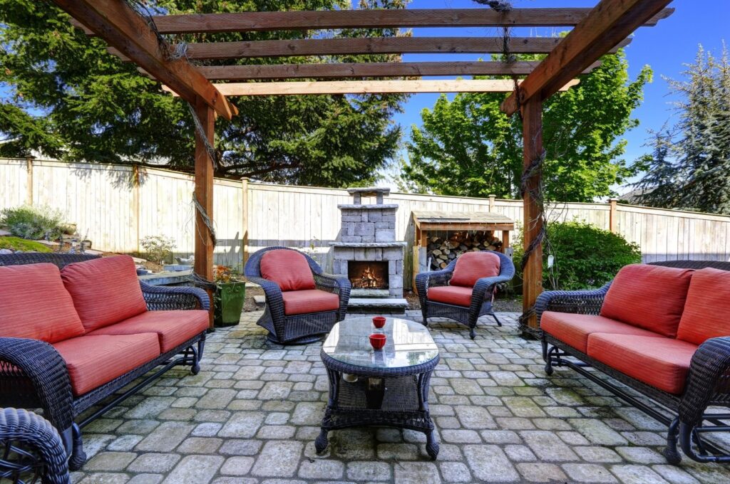 Timber pergola over an outdoor lounge setting with a stone fireplace and wicker furniture