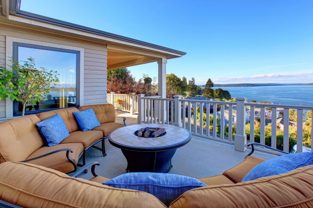 Covered patio with lounge seating and a fire pit table overlooking a waterfront view