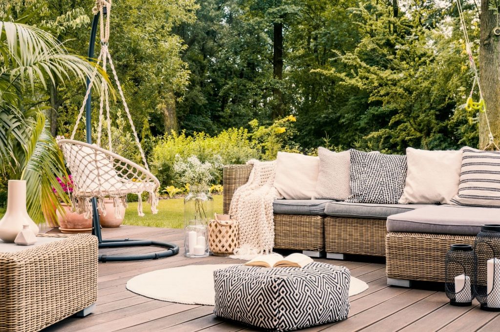 Outdoor lounge patio with wicker furniture, a hanging chair and garden greenery